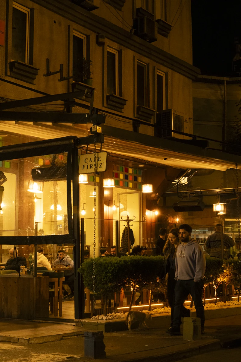 Cafe Firuz at night: the lit garden and guests walking by