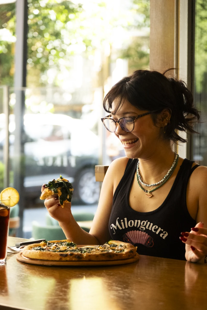 A smiling guest eating pizza by the window